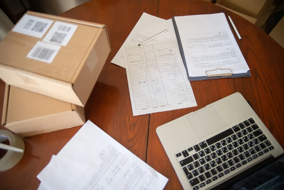 Shipping paperwork, labelled parcels and a laptop on a desk